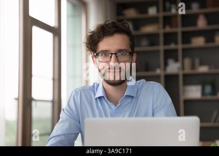 Happy millennial man worker look at camera above notebook screen Stock Photo