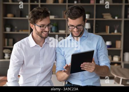 Two smiling young twin brothers using tablet in living room Stock Photo