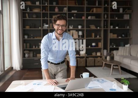 Happy young male entrepreneur standing at desk looking at camera Stock Photo