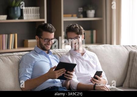 Two young twin brothers share information between tablet and smartphone Stock Photo