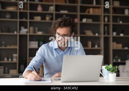 Concentrated young male student handwriting at work desk using notebook Stock Photo