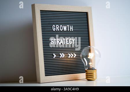 An image showcasing a light bulb beside a message board displaying 'Growth Strategy', innovative business development, progress, and planning concepts Stock Photo