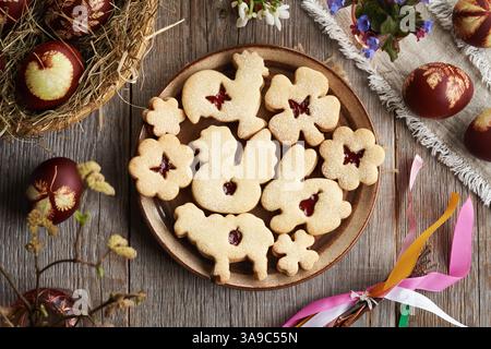 Animal shaped Linzer Easter cookies on a plate with Easter eggs dyed with onion peels, top view Stock Photo