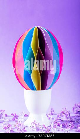 Decorative paper Easter egg in an egg cup and lilac flowers on a lilac background. Easter idea, selective focus. Stock Photo
