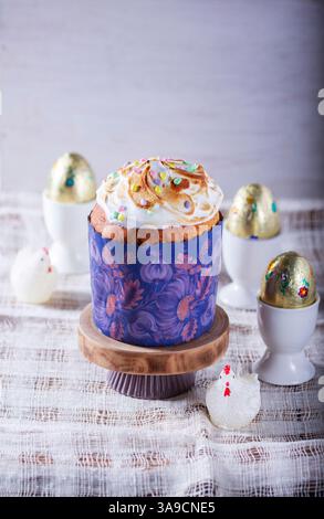 Easter cake, chocolate eggs in gold foil and chicken-shaped candles on a light background. Traditional Easter cake with meringue and colored sugar dec Stock Photo