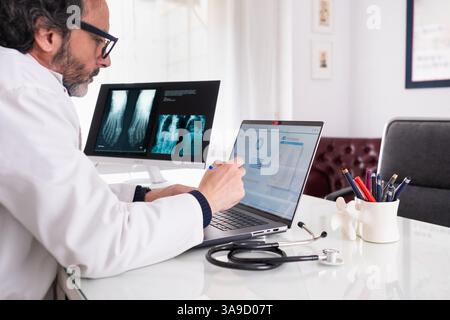 A middle-aged doctor wearing a white coat studies a case using generic anonymous healthcare software. In the background, there is another screen with Stock Photo