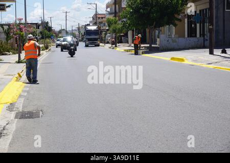 Two workers in fluorescent vests hold brushes and paint the curb edges with yellow paint on a street Stock Photo
