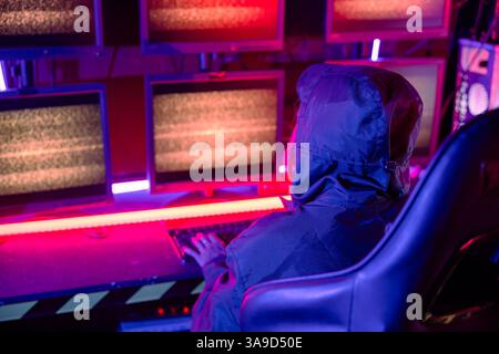 Woman hacker wear hood sit front computer typing on keyboard hacking servers in neon light, Gamer Stock Photo