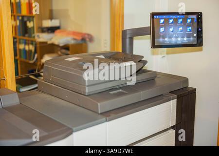 Close up view of office photocopier with control panel and bookshelf in blurred background. Sweden. Stock Photo