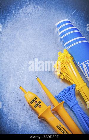 Yellow electrical tester self-locking cable ties blue construction plans on metallic background electricity concept Stock Photo
