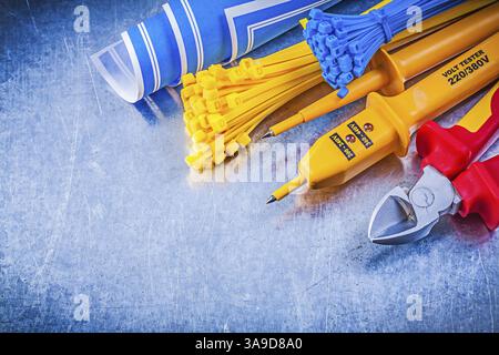 Yellow electrical tester self-locking cable ties blue blueprints nippers on metallic background electricity concept Stock Photo