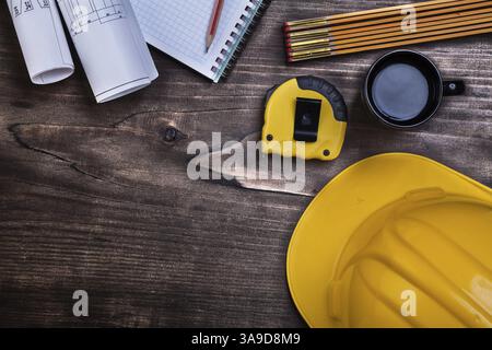 Workbook pencil blueprints instruments of measurement construction helmet and coffee on wooden board Stock Photo