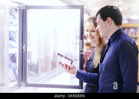 Couple in the frozen goods section of a grocery store picking out food from the freezer Stock Photo