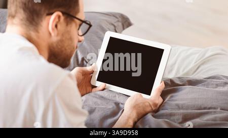 Man Using Digital Tablet With Empty Screen Lying In Bed Stock Photo