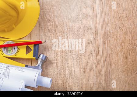 Yellow hardhat rolled white blueprints level red pencil and claw hammer on wooden board copyspace construction concept background Stock Photo