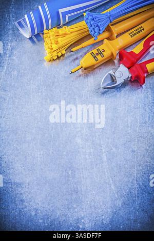 Yellow electrical tester self-locking tying cables blue blueprints nippers on metallic background electricity concept Stock Photo