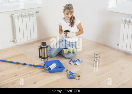 Horizontal ersion a young beautiful female painter sitting on the floor drinlking coffee and think with color palette Stock Photo