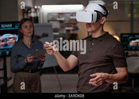 Focus on young man with VR headset making virtual presentation of new project while pressing button on remote control Stock Photo
