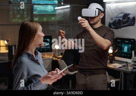Focus on young male engineer wearing VR headset pressing button on remote control while presenting new model of car Stock Photo