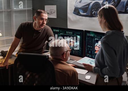 Group of three modern designers having discussion of new project points at working meeting in front of computer screens Stock Photo