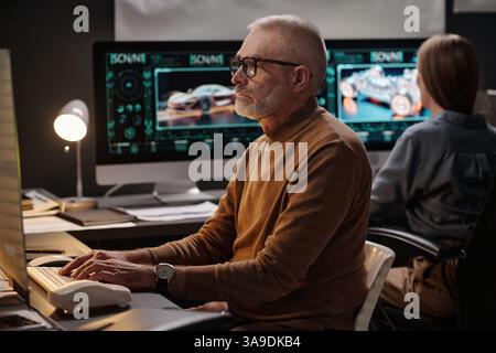 Serious mature male engineer looking at computer screen and pressing keys of keyboard while working over creative project Stock Photo