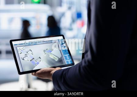 Technician in solar panel facility reviewing photovoltaic system performance on tablet. Close up of specialist analyzing production metrics on device to optimize efficiency in industrial plant Stock Photo