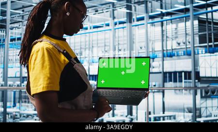 Smart factory specialist using mockup laptop to test automated systems and ensure reliability. Woman uses isolated screen notebook to identify bottlenecks and optimize equipment, camera A Stock Photo