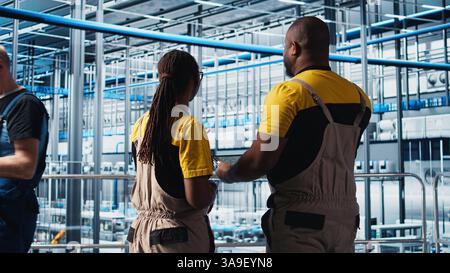 Industry 4.0 industrial plant engineering team controlling automated machinery using tablet, ensuring workflow continuity. Teamworking smart factory colleagues manage robotic arms, camera A Stock Photo