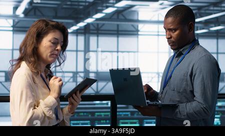 System administrators using notebook device in data center, managing server virtualization. IT specialists using laptop in server farm, sustaining long term infrastructure reliability, camera A Stock Photo