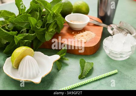Wooden cutting board, juicer and ingredients for mojito on green background, closeup Stock Photo