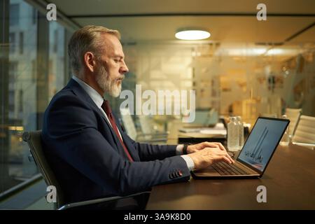 Mature Caucasian architect working on laptop with modern building design on screen, side view Stock Photo