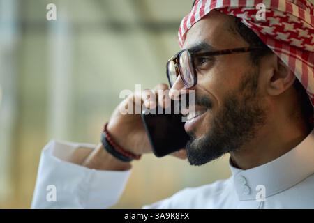 Closeup of confident young Middle Eastern male CEO in eyeglasses talking on phone, copy space Stock Photo
