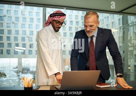 Diverse male entrepreneurs using laptop while discussing new business project in modern office, copy space Stock Photo