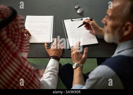 High angle view over shoulder shot of two ethnically diverse colleagues discussing agreement documents Stock Photo