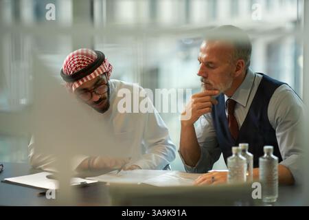 Through glass wall of two ethnically diverse young and mature colleagues working with documents together in modern office Stock Photo