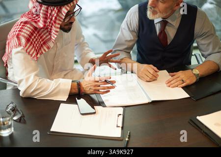 High angle view of two diverse male managers sitting at desk in office, reading and discussing documents Stock Photo