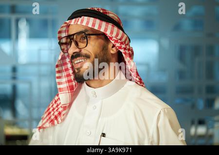 Portrait of cheerful Middle Eastern male entrepreneur in traditional attire standing in modern office Stock Photo