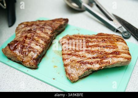 Two juicy grilled flank steaks with char lines placed on a green cutting board, ready for slicing and serving. Stock Photo