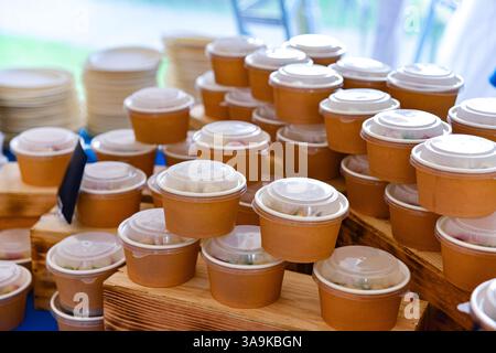 Multiple brown paper food containers with plastic lids neatly arranged on wooden stands, ready for distribution at a catered event. Stock Photo