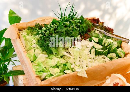 A wooden box filled with fresh chopped lettuce, cucumbers, cabbage, dill, cilantro, and other leafy greens for a healthy salad. Stock Photo