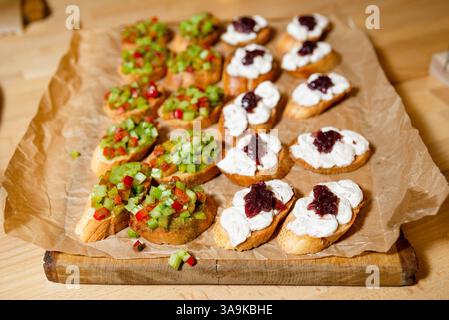 A tray of assorted bruschetta appetizers topped with creamy spread and jam, and diced vegetables on toasted bread slices. Stock Photo