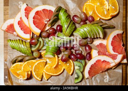 Vibrant assortment of fresh sliced fruits including oranges, grapefruit, pears, kiwi, and grapes arranged on parchment for serving. Stock Photo