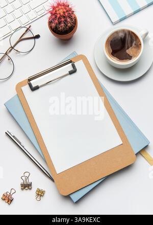 Home office desk workspace with blank clipboard, keyboard, coffee, cactus, glasses, pen, notebook, and binder clips, inviting creativity and productiv Stock Photo