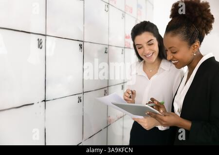 Happy diverse female office colleagues using tablet at scrum Stock Photo