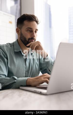 Focused pensive handsome Latin businessman working at laptop in office Stock Photo