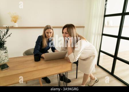 Two women collaborating on a project while discussing plans in a modern workspace during the day Stock Photo
