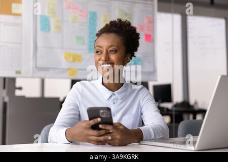 Cheerful positive young African manager woman using smartphone in office Stock Photo