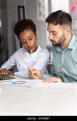Two young diverse managers analyzing marketing report at office table Stock Photo