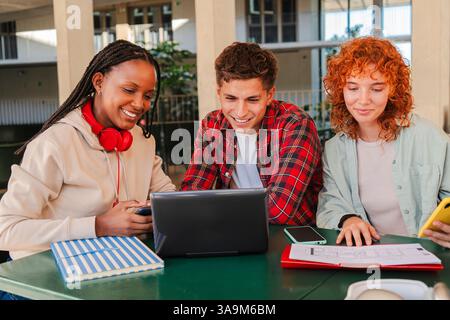 A dynamic trio of motivated students working together on a laptop, sharing knowledge and insights, while enjoying each other's company and fostering a spirit of teamwork in an academic environment filled with excitement Stock Photo