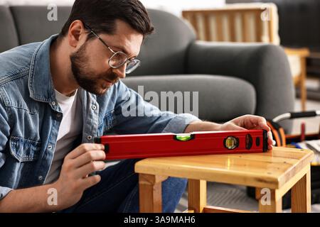 Man using level tool while repairing wooden stool at home Stock Photo
